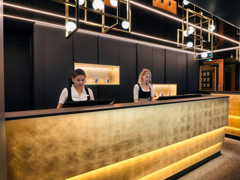 Die Rezeption im Hotel Oswald mit freundlichem Empfangsteam, stilvollem Design und warm beleuchtetem Tresen für eine einladende Atmosphäre.
